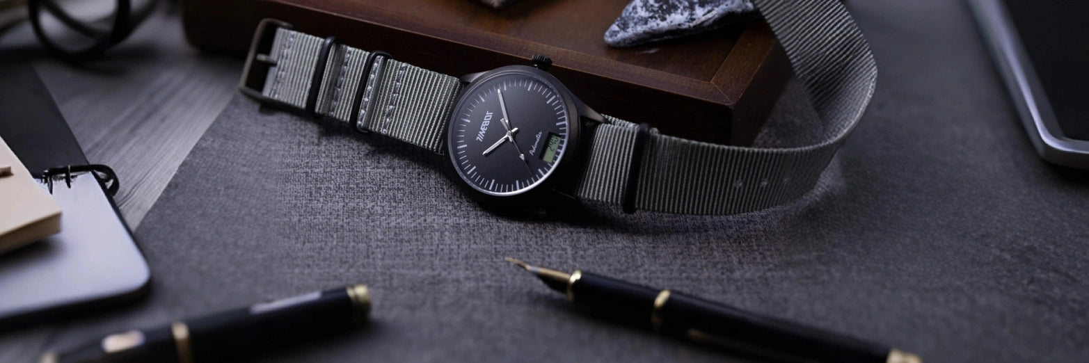 Timebot T591C1 Black pedometer watch with mesh strap on a dark surface with pens and a phone