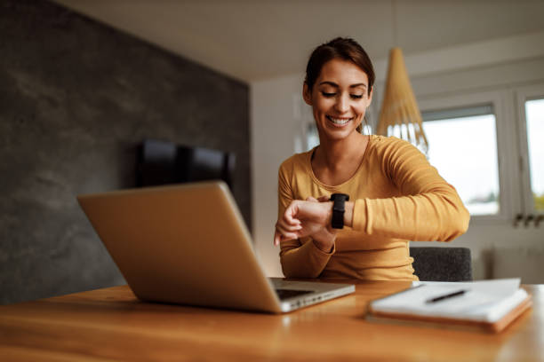 Woman using a laptop and checking her steps on a timebot watch in a home setting