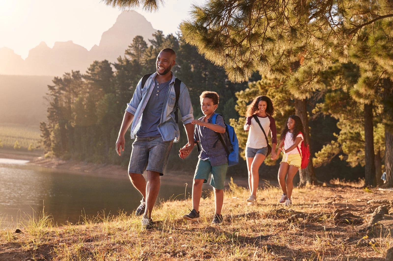 Family of four walking along a trail near a lake with mountains in the background